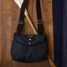 Load image into Gallery viewer, Navy blue bag with straps hanging on a wooden door.
