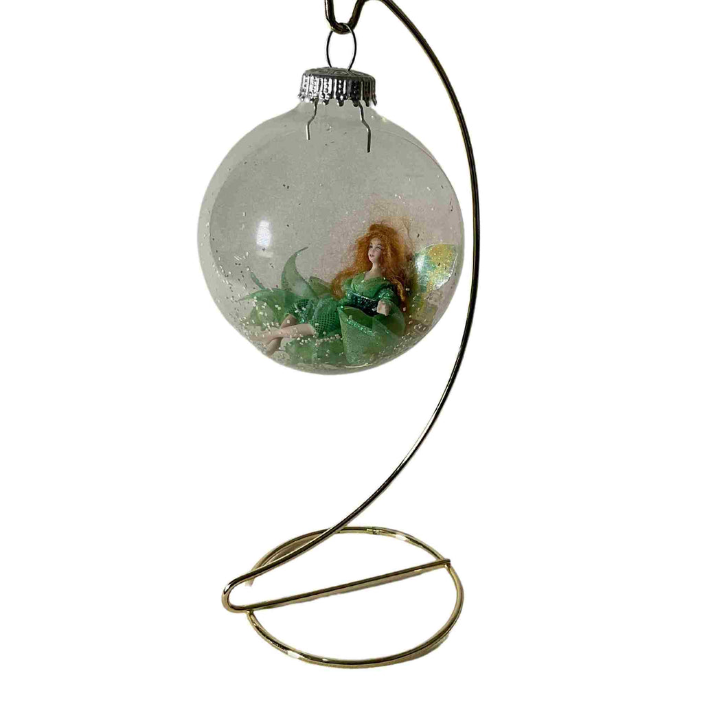 Laying green miniature fairy inside a clear snowy hanging ornamental ball.