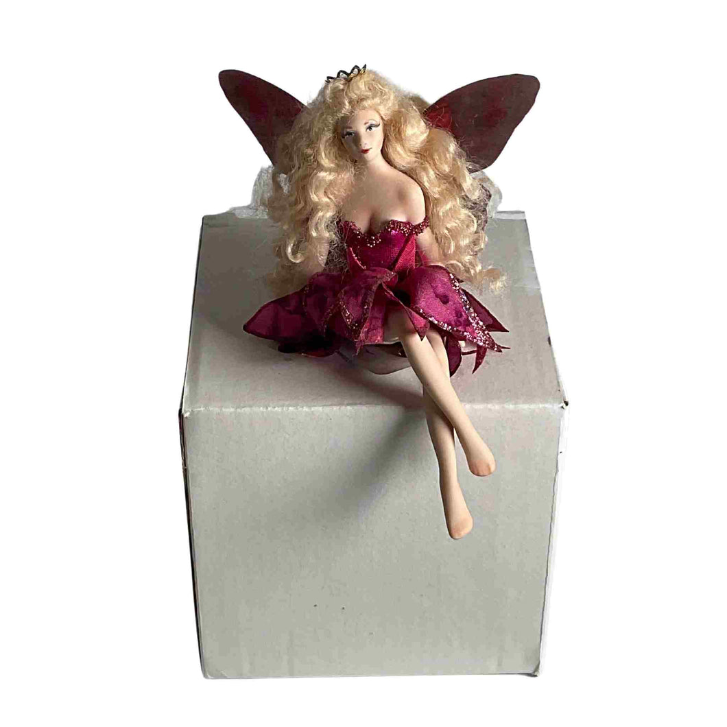 Sitting handmade porcelain fairy dressed in a wine coloured dress.